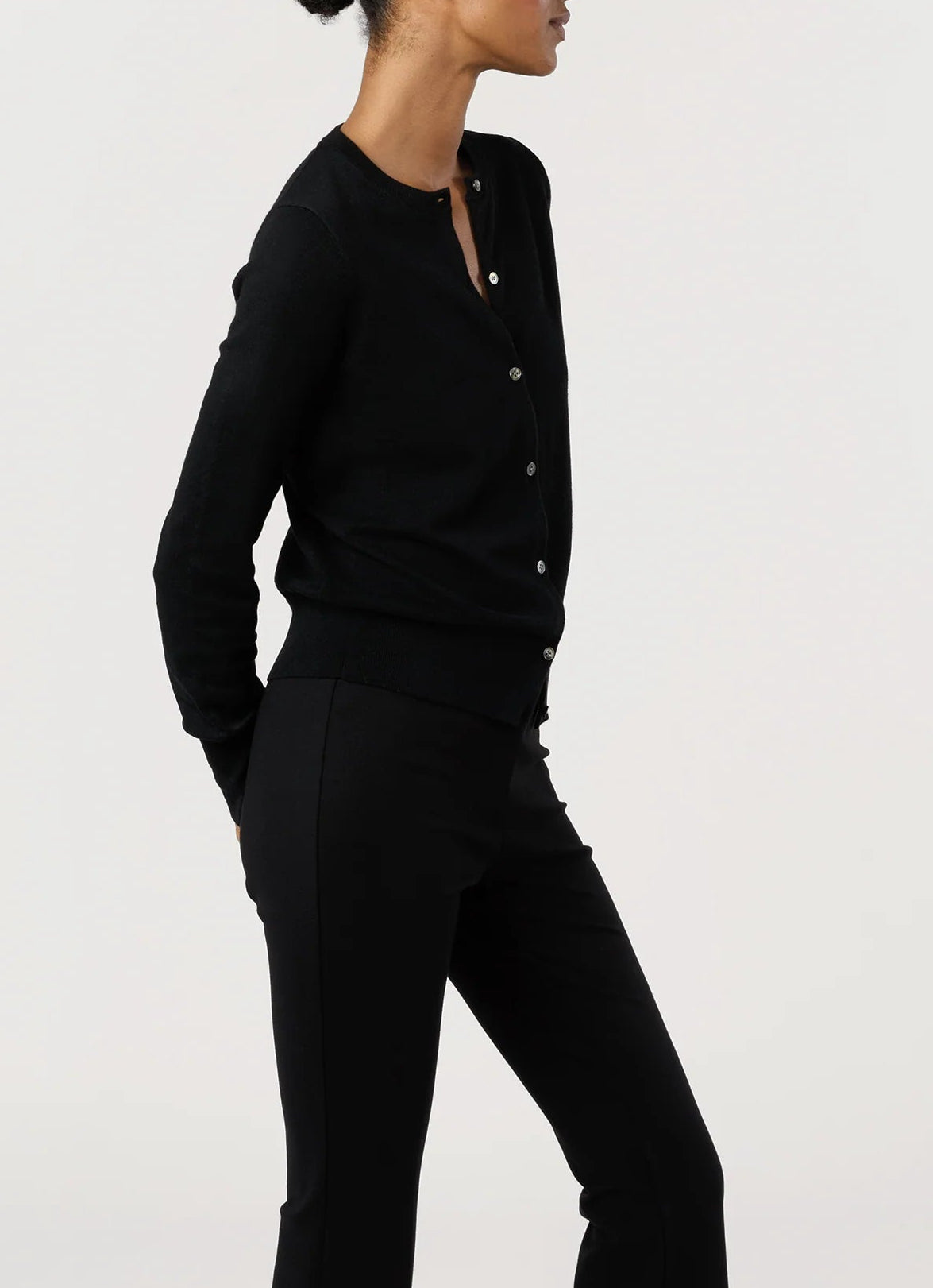 A person wears the Ann Mashburn Rosie Cotton Silk Cardigan in black with black pants, standing sideways against a plain light background, arms relaxed behind their back.