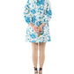 A person in the Ann Mashburn Francine Dress—white faille with blue floral print—faces away, holding a small yellow flower behind their back and wearing wedge sandals.