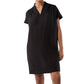 A person models the Ann Mashburn Libby Dress, a short-sleeve, knee-length black V-neck design, standing against a plain background.