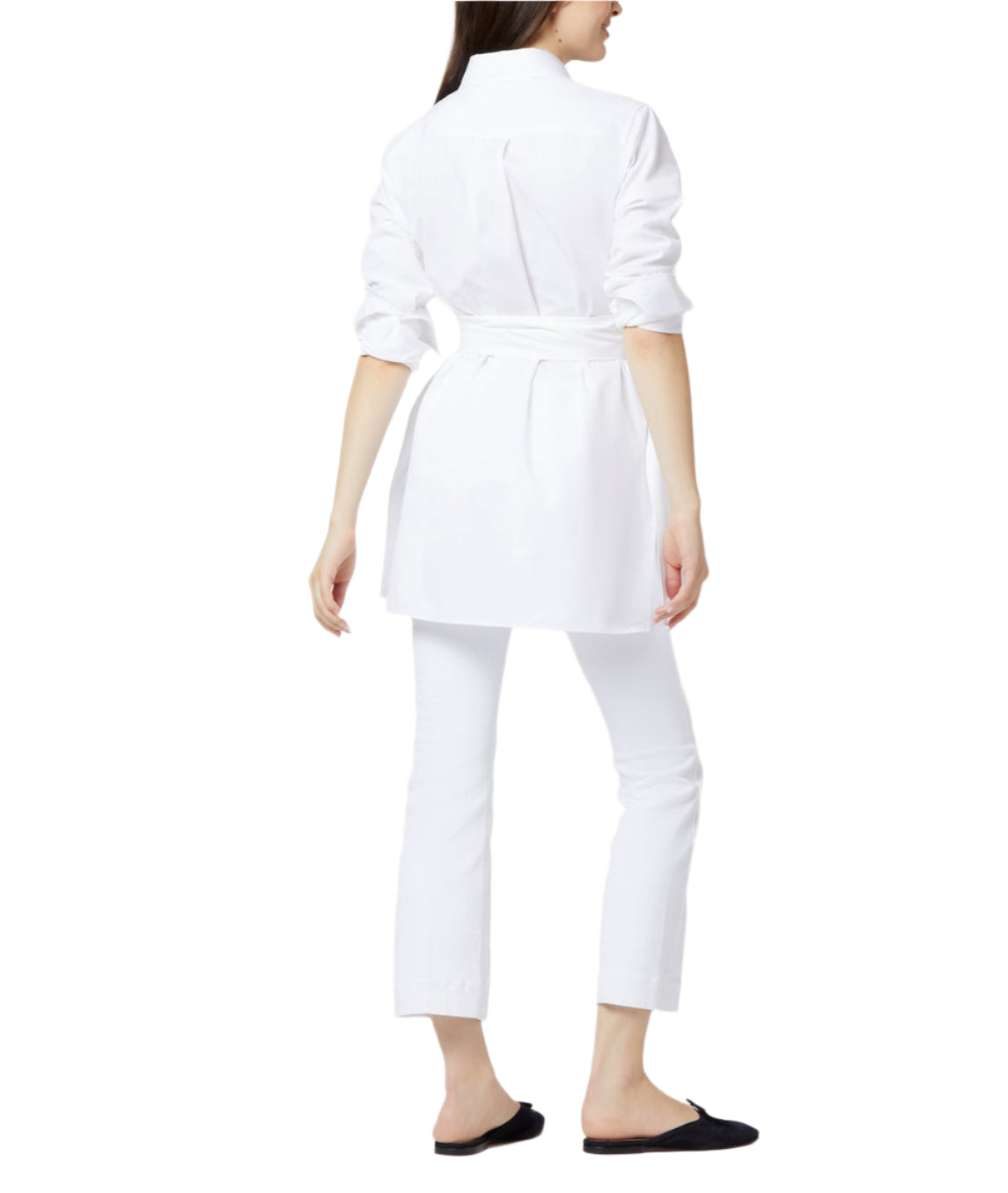 A woman stands with her back to the camera, wearing the Ann Mashburn Gabrielle Tie Tunic in white Italian poplin, accented at the waist, paired with white slim-fit pants and black flats against a white background.