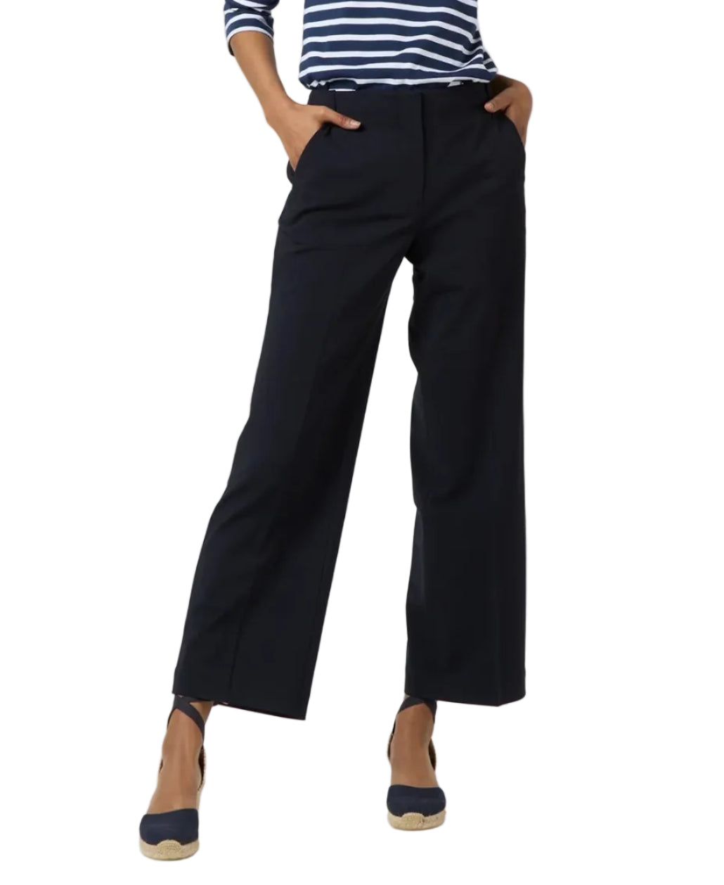 A person wears Ann Mashburn's Frankie Cropped Bi-Stretch Tropical Wool Pant with a Hollywood waistband, a navy and white striped long-sleeve top, and black espadrille wedges, standing with hands in their pockets.