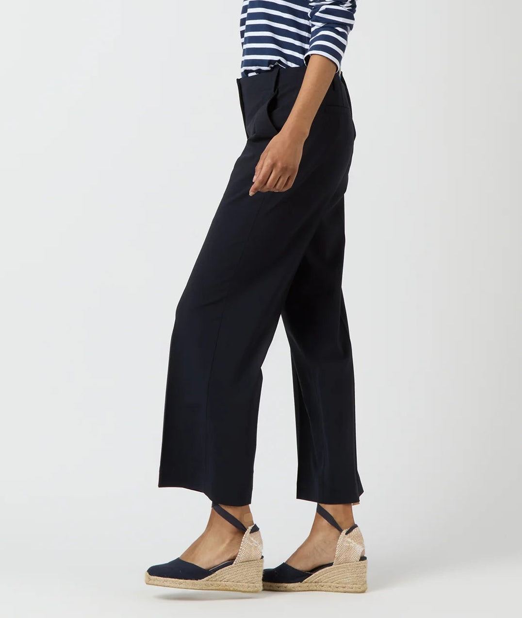 A person in a navy striped top, Ann Mashburn Frankie Cropped Bi-Stretch Tropical Wool Pant, and navy espadrille wedge sandals stands against a plain light background.