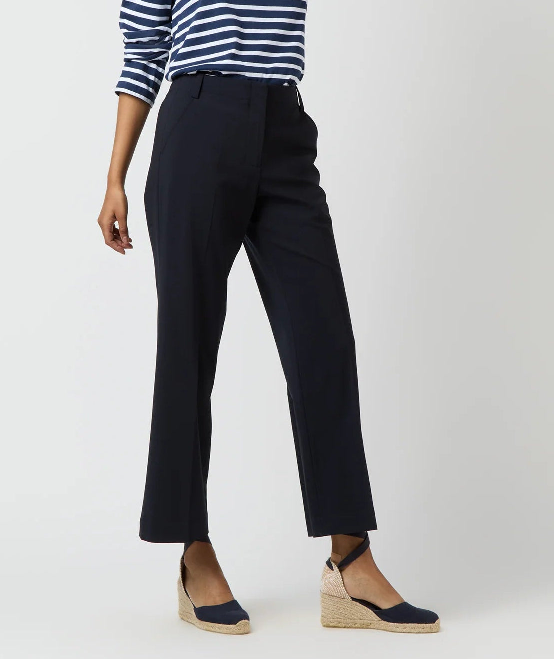 A person in Ann Mashburn’s Frankie Cropped Bi-Stretch Tropical Wool Pant, a navy striped top, and navy espadrille wedge shoes stands against a plain light background.