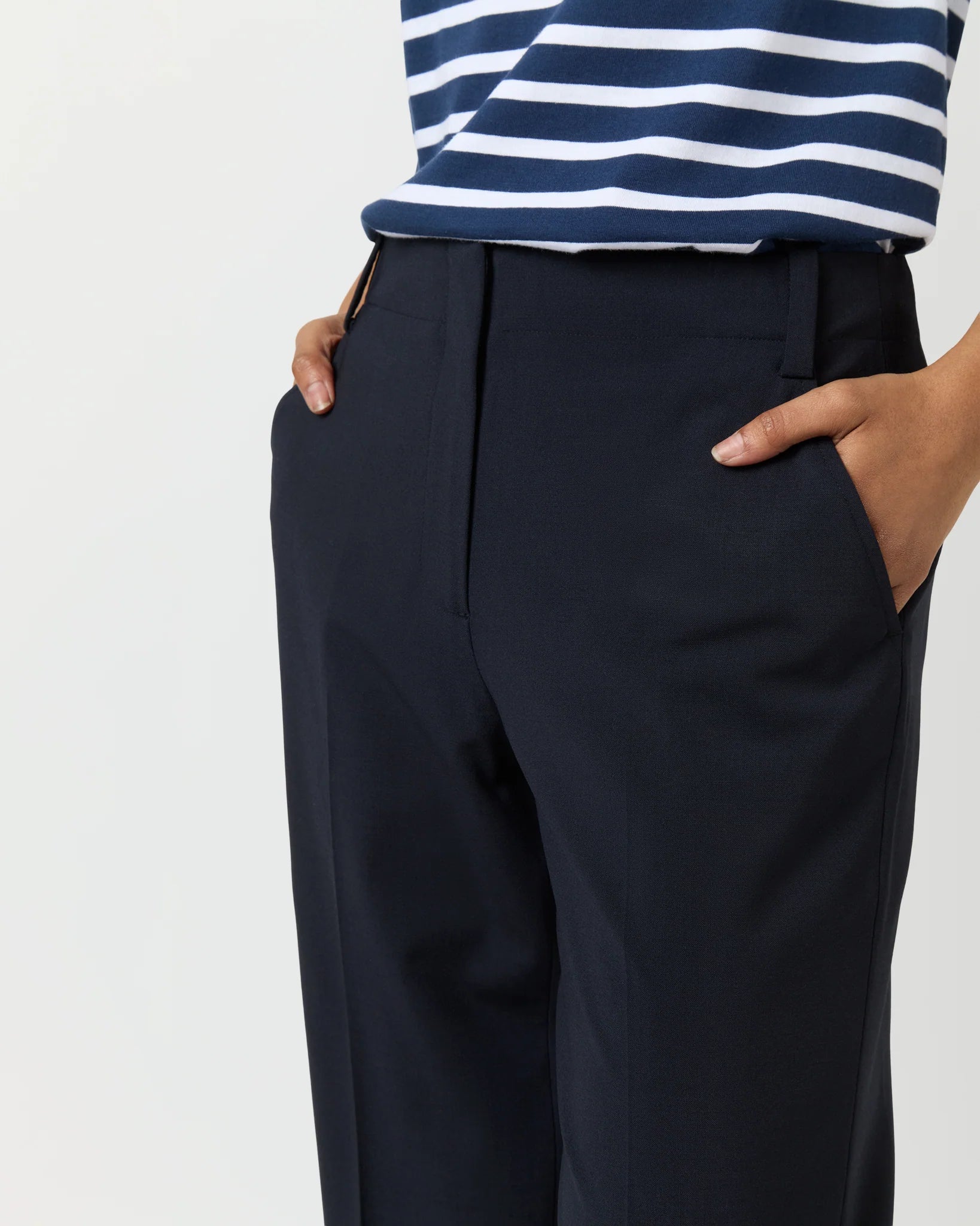 Person wearing the Ann Mashburn Frankie Cropped Bi-Stretch Tropical Wool Pant in dark navy with a relaxed fit, paired with a navy and white striped shirt, hands in pockets, shown from shoulders to knees.