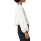 A woman in side profile wears the Ann Mashburn Ariana Blouse with balloon sleeves and black pants, set against a white background.