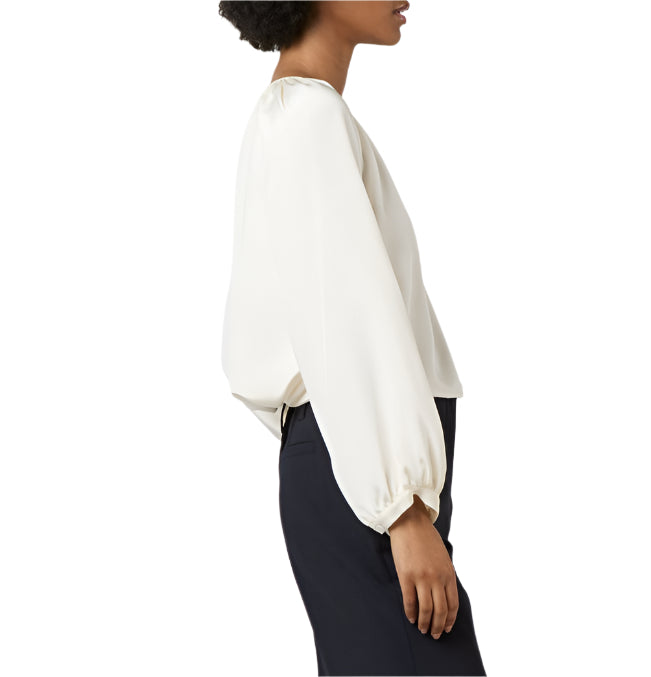 A woman in side profile wears the Ann Mashburn Ariana Blouse with balloon sleeves and black pants, set against a white background.