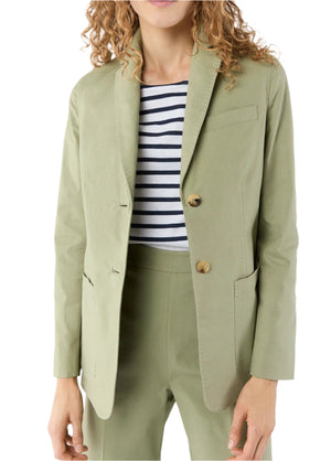 A woman stands against a white background wearing the Ann Mashburn Sarah Stretch Canvas Jacket in light green with matching trousers and a black-and-white striped shirt underneath.