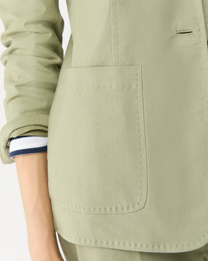 Close-up of a person wearing the Ann Mashburn Sarah Stretch Canvas Jacket in light green, featuring a large front pocket and rolled-up sleeves that reveal a white shirt cuff with a navy stripe.