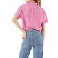 A person stands with one hand on their hip, wearing the Ann Mashburn Agnes Shirt—an oversized pink short-sleeve striped top—and light blue jeans, viewed from the back.