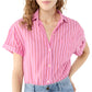Someone is wearing the Ann Mashburn Agnes Shirt—a pink and red vertically striped, oversized short-sleeve button-up with Trocas shell buttons—paired with light blue jeans.