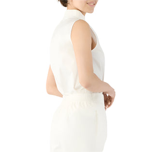 A person wearing the Ann Mashburn Clair Top—a sleeveless, white crisp poplin blouse—paired with white high-waisted pants, shown in profile against a white background.