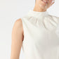 A person wears the Clair Top by Ann Mashburn, a sleeveless white mock neck tank in crisp poplin with a high pleated collar, shown from the shoulders up against a plain light background.