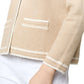 A close-up shows a person in the Aubrey Cardigan by Ann Mashburn, featuring hand-crocheted trim on the arm, crafted from a luxurious cotton/silk blend. The garment is in beige with white trim and paired with white pants, highlighting its elegant side view.