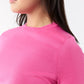 A person with long dark hair wears the Ann Mashburn Lee Tee in bright pink, featuring a body-hugging fit, shown from the shoulders up against a plain background.
