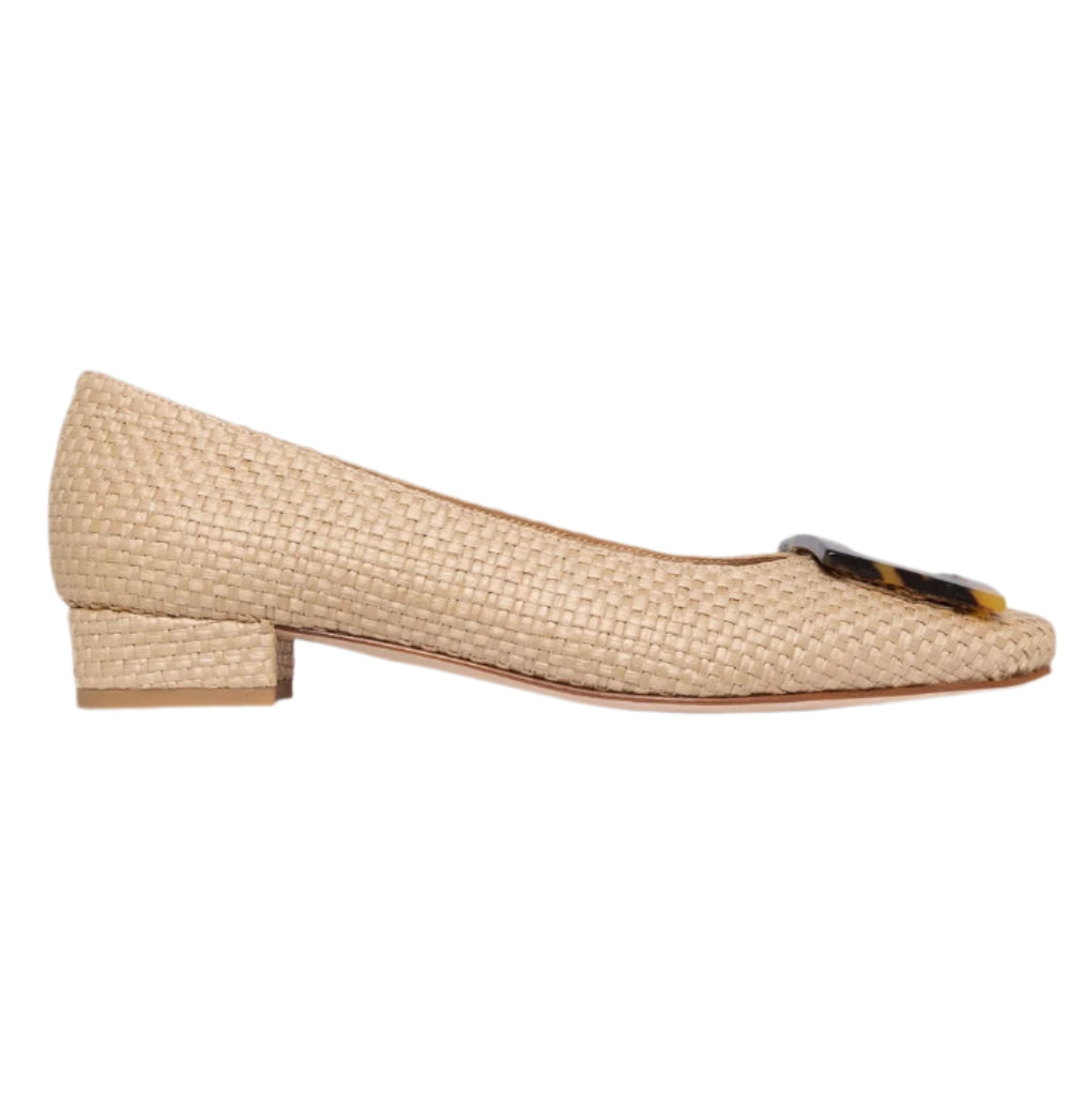 The Ann Mashburn Buckle Basketweave Shoe features a beige woven design with a low block heel and dark toe accent, evoking subtle 1960s style. Shown in profile on a white background.