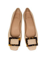 The Ann Mashburn Buckle Basketweave Shoe is a pair of beige woven flats with square tortoiseshell buckles on the toes, inspired by 1960s style and shown from above.