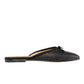 The Ann Mashburn Joy Basketweave Mule is a black woven slip-on with a flat sole, elegant small bow, and almond-shaped toe box with a pointed finish. Made in Italy and showcased from the side on a pristine white background.