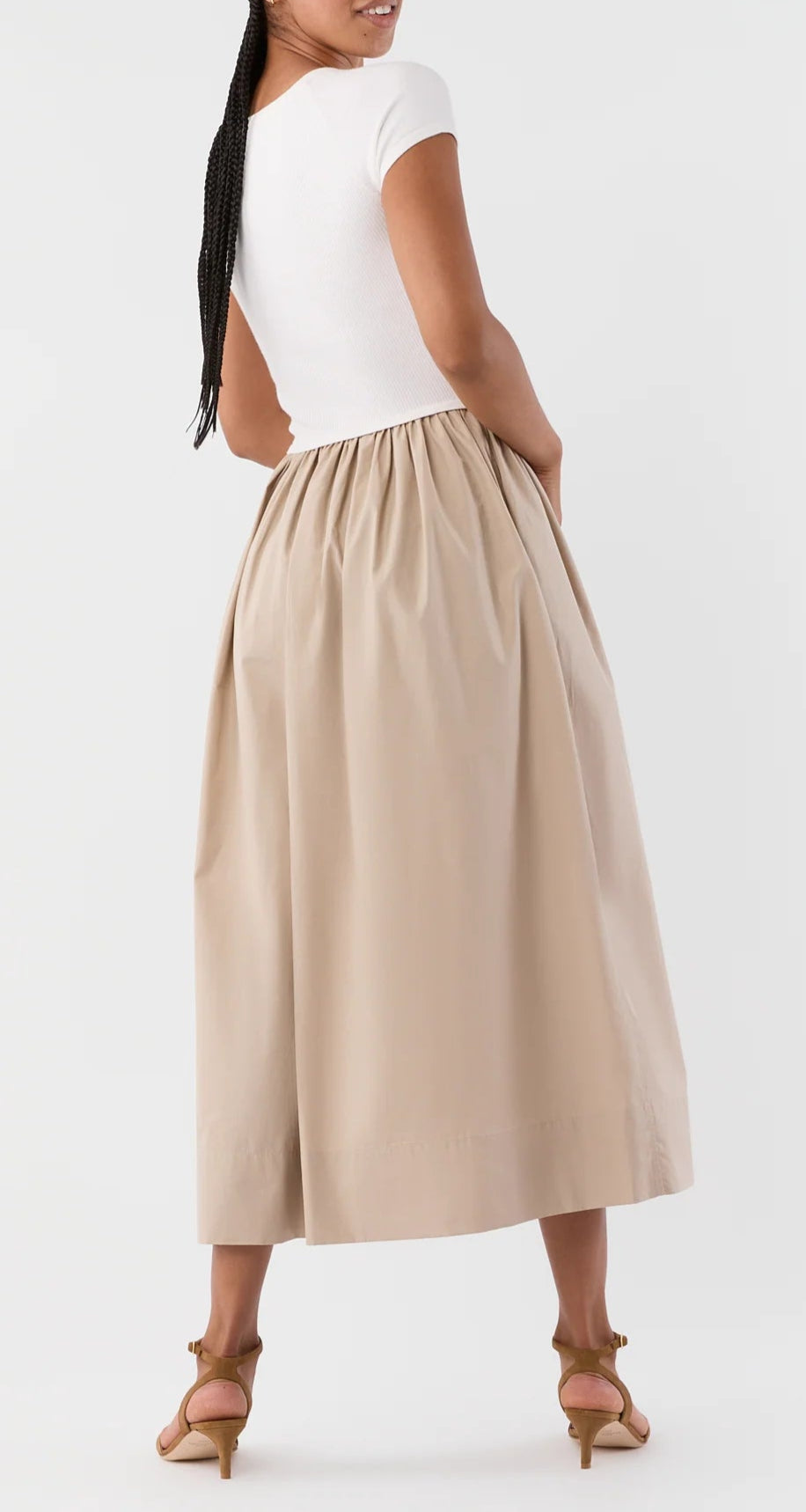 A woman stands facing away, wearing the Cosette Cotton Silk Dress by Ann Mashburn and tan heeled sandals against a plain background.