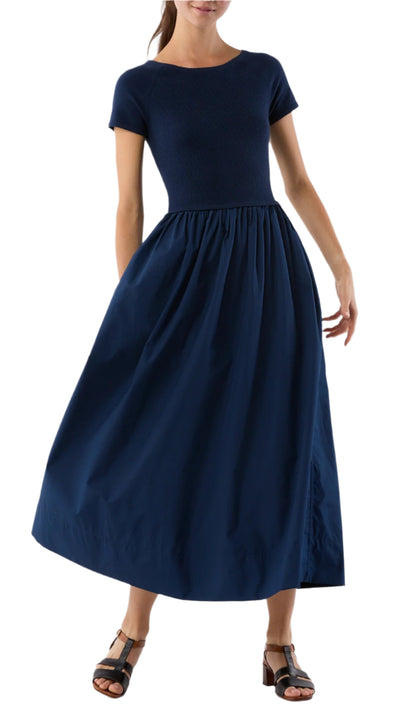 A woman wears the Ann Mashburn Cosette Cotton Silk Dress, featuring a fitted bodice and full poplin skirt in navy blue, paired with black sandals.