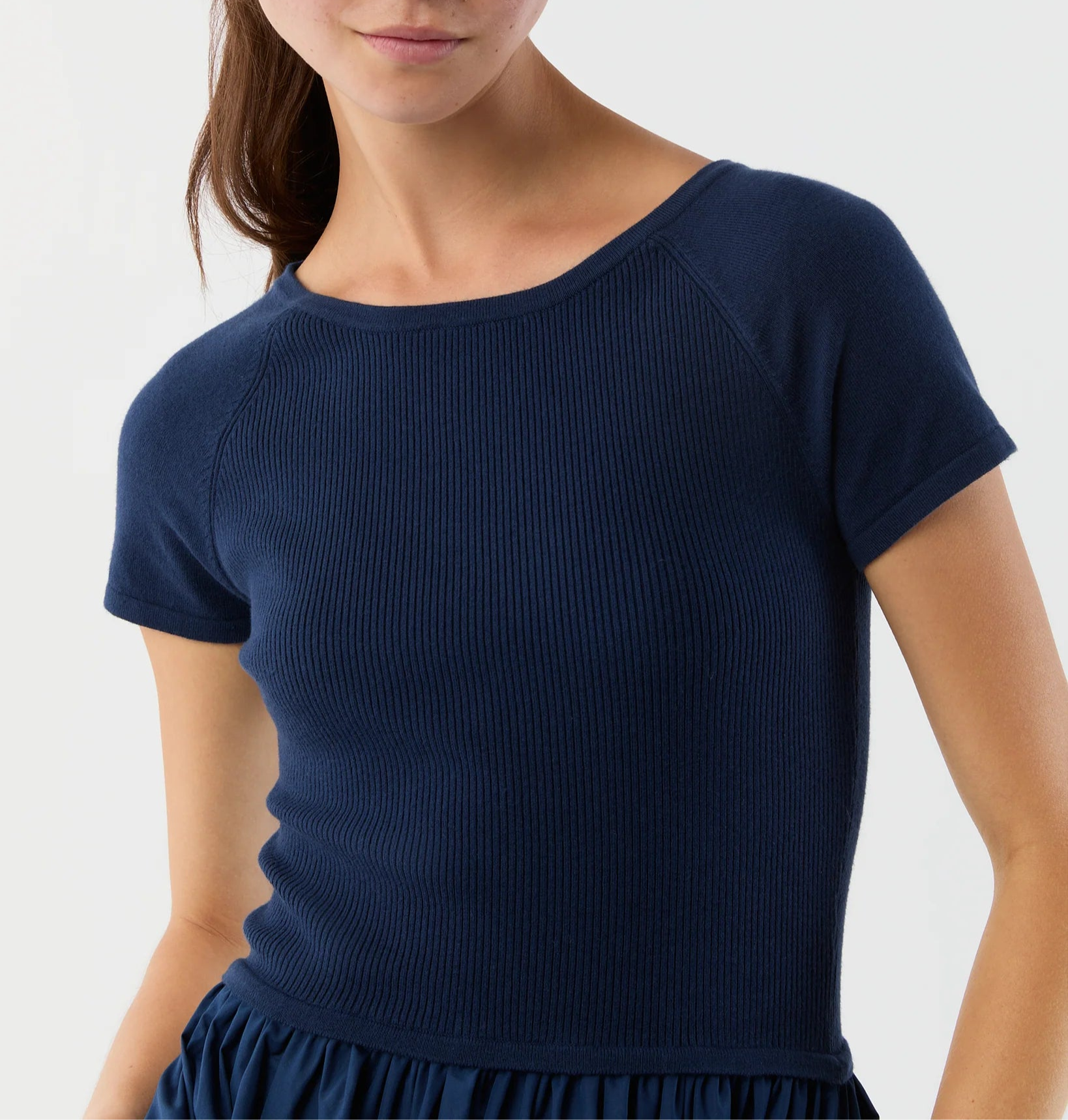 A woman in the Ann Mashburn Cosette Cotton Silk Dress, a short-sleeved ribbed navy blue knit with round neck, styled with a gathered poplin skirt.