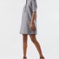 A woman wears the Ann Mashburn Elbow Sleeve Frill Dress, a feminine knee-length black-and-white checkered piece with a standing collar and front buttons, paired with black strappy heels and a neatly finished hem.