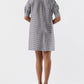 A woman faces away, wearing the Ann Mashburn Elbow Sleeve Frill Dress—a feminine black and white checkered short dress with elbow-length sleeves—paired with black heeled sandals against a plain white background.