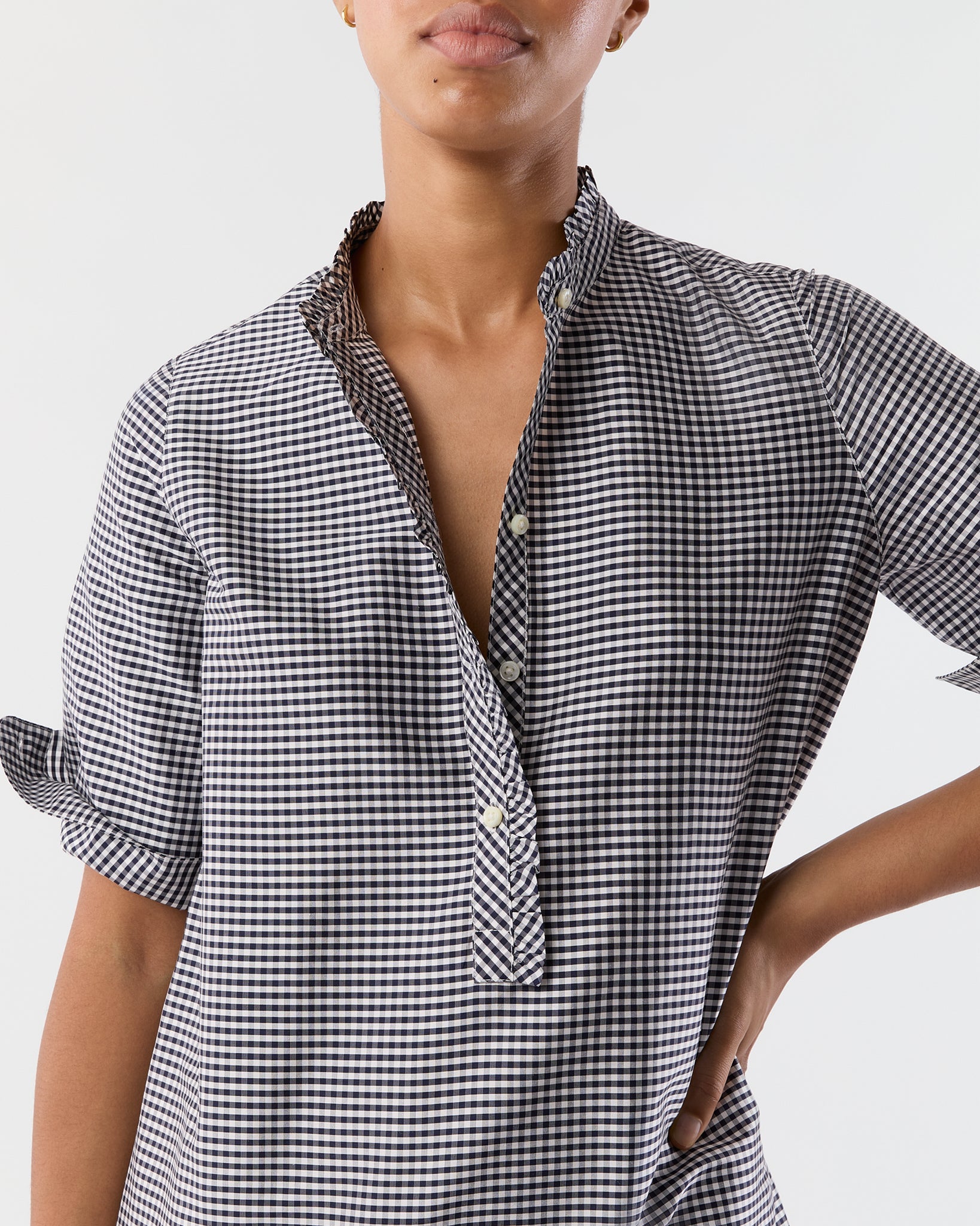 A person stands against a plain white background wearing the Ann Mashburn Elbow Sleeve Frill Dress in a black-and-white checkered pattern.