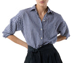 A person wears the Ann Mashburn Weekender Shirt in blue and white checks, sleeves rolled up and tucked into a high-waisted black skirt for a relaxed look.