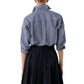 A person faces away from the camera in an Ann Mashburn Weekender Shirt—blue and white checks with rolled-up sleeves—paired with a black pleated skirt for a relaxed silhouette.