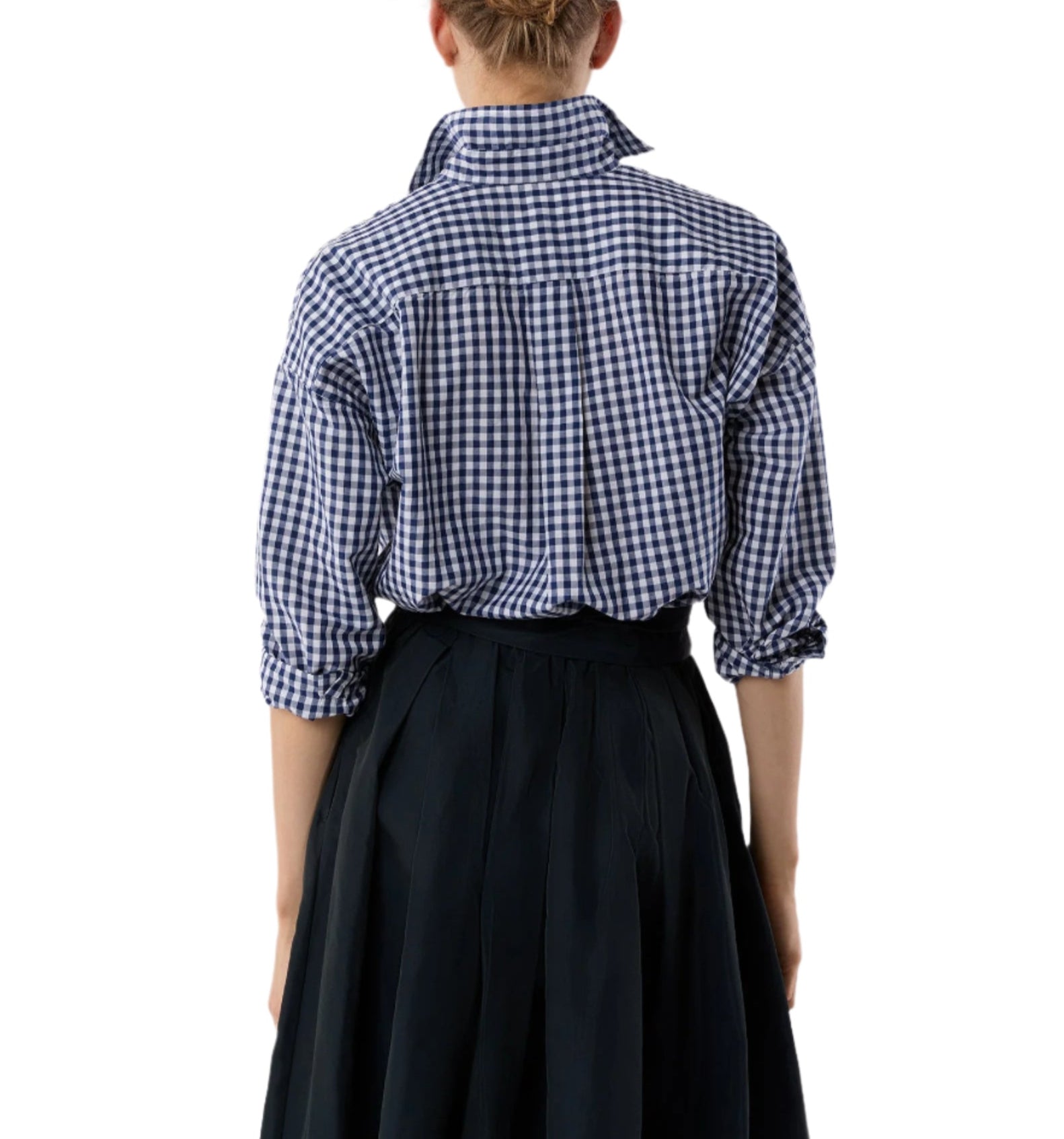 A person faces away from the camera in an Ann Mashburn Weekender Shirt—blue and white checks with rolled-up sleeves—paired with a black pleated skirt for a relaxed silhouette.