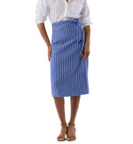 A person wearing a white button-up shirt, Ann Mashburn’s Kara Wrap Skirt in blue and white stretch jacquard, and tan strappy sandals stands against a white background.