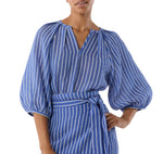 A woman wears the Ann Mashburn Victoria Blouse, featuring blue and white vertical stripes, balloon sleeves, and stretch jacquard fabric with a matching waist tie belt.