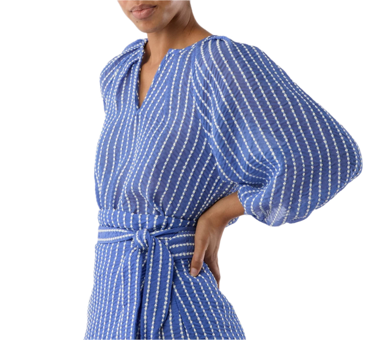 A woman in the Ann Mashburn Victoria Blouse—a blue and white striped top with balloon sleeves, romantic details, and a matching waist tie—stands with one hand on her hip.