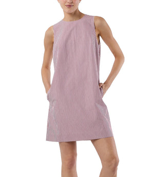 A person wears the Ann Mashburn Susy Shift Dress, a sleeveless, knee-length 1960s-style A-line with vertical red and white stripes, standing with one hand in a pocket for a polished look.