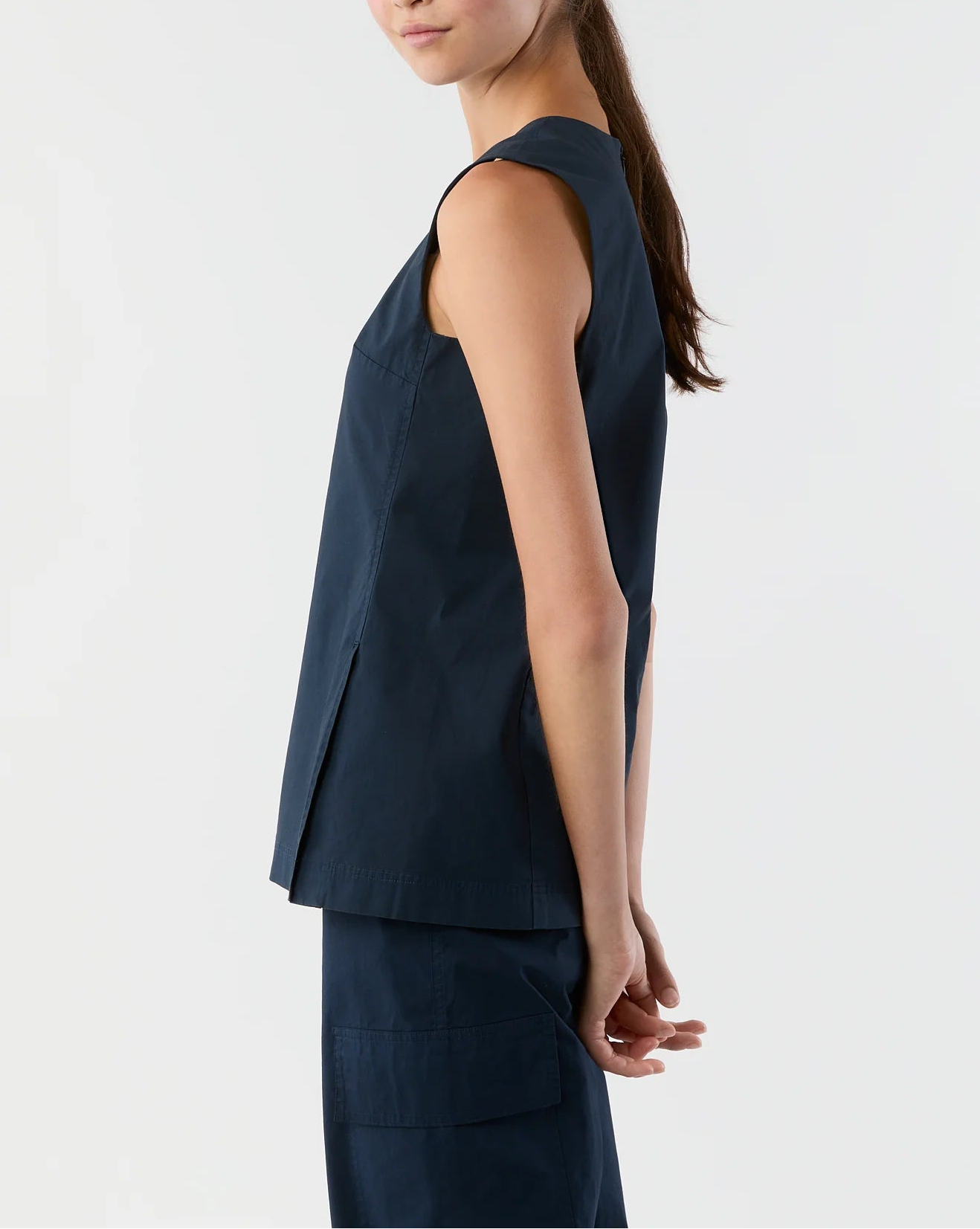 A woman stands sideways against a plain background, hands behind her back, wearing the Ann Mashburn Jo Bi-Stretch Tropical Wool Tunic and matching navy pants.
