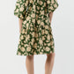 A person shown from the back wears the Ann Mashburn Allegra Dress in green seersucker with beige floral patterns and a tiered skirt, paired with brown heeled sandals, against a plain background.