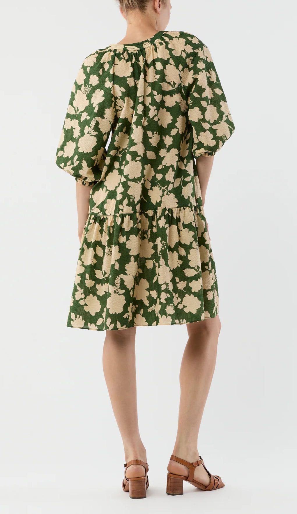 A person shown from the back wears the Ann Mashburn Allegra Dress in green seersucker with beige floral patterns and a tiered skirt, paired with brown heeled sandals, against a plain background.