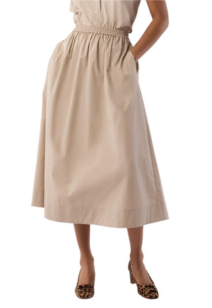 A person wears the Ann Mashburn Miranda Poplin Skirt in beige, high-waisted with pockets and a midi hem, styled with leopard print heels and shown from shoulders to feet.