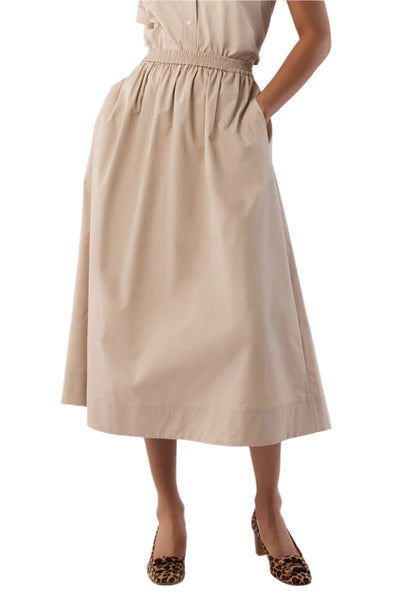 A person wears the Ann Mashburn Miranda Poplin Skirt in beige, high-waisted with pockets and a midi hem, styled with leopard print heels and shown from shoulders to feet.