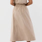 A person stands facing away, wearing the Ann Mashburn Miranda Poplin Skirt in tan with an elastic waist and a midi hem, paired with brown leopard-print heeled sandals.