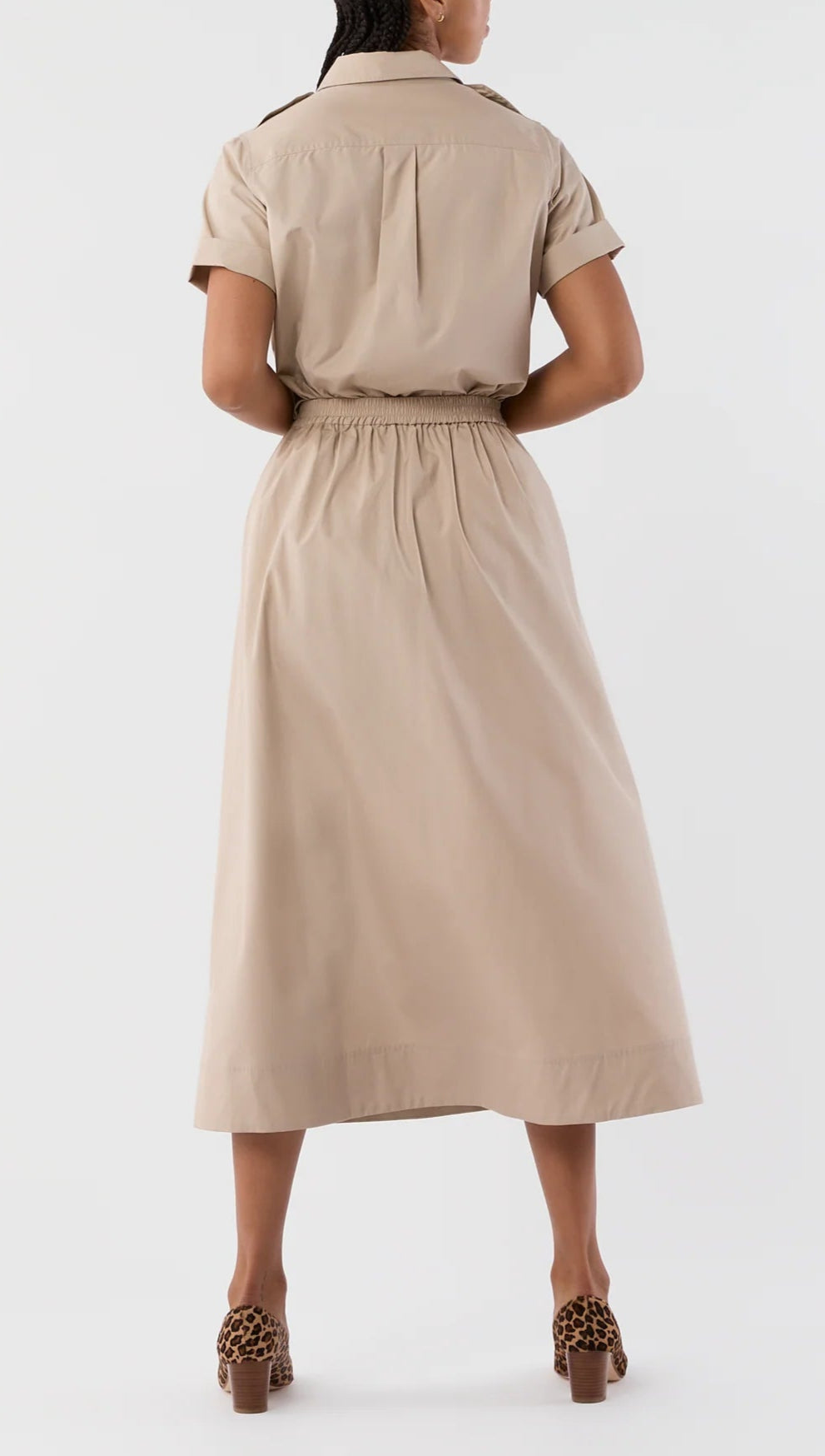 A person stands facing away, wearing the Ann Mashburn Miranda Poplin Skirt in tan with an elastic waist and a midi hem, paired with brown leopard-print heeled sandals.