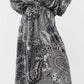 A person wearing the Ann Mashburn Sienna Block Print Top, featuring a black and white abstract botanical print, styled with black heeled sandals for a refined romantic look.
