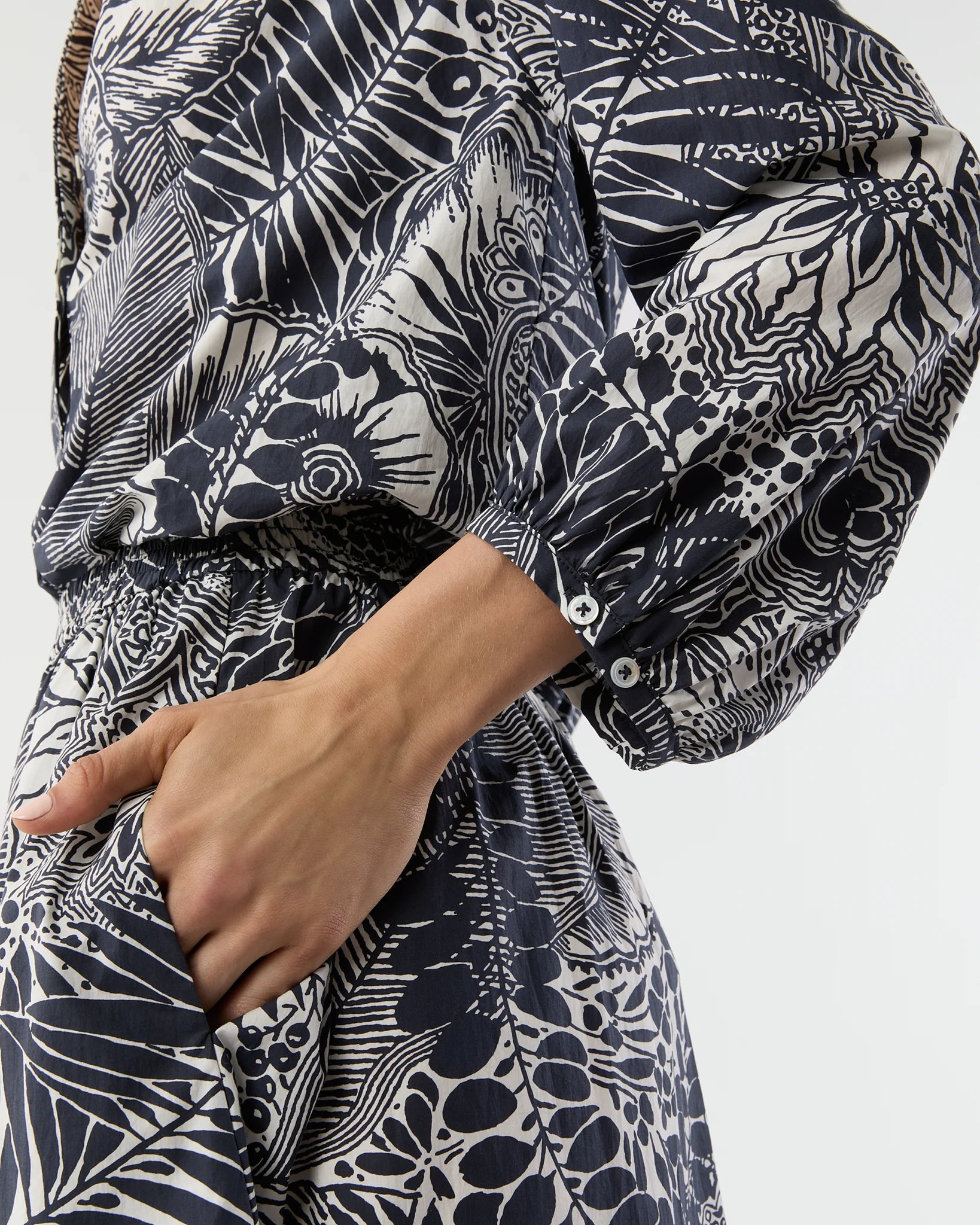 A person wearing the Ann Mashburn Sienna Block Print Top, a long-sleeved romantic style with a monochrome botanical pattern, shown from neck to mid-thigh with one hand in a pocket.