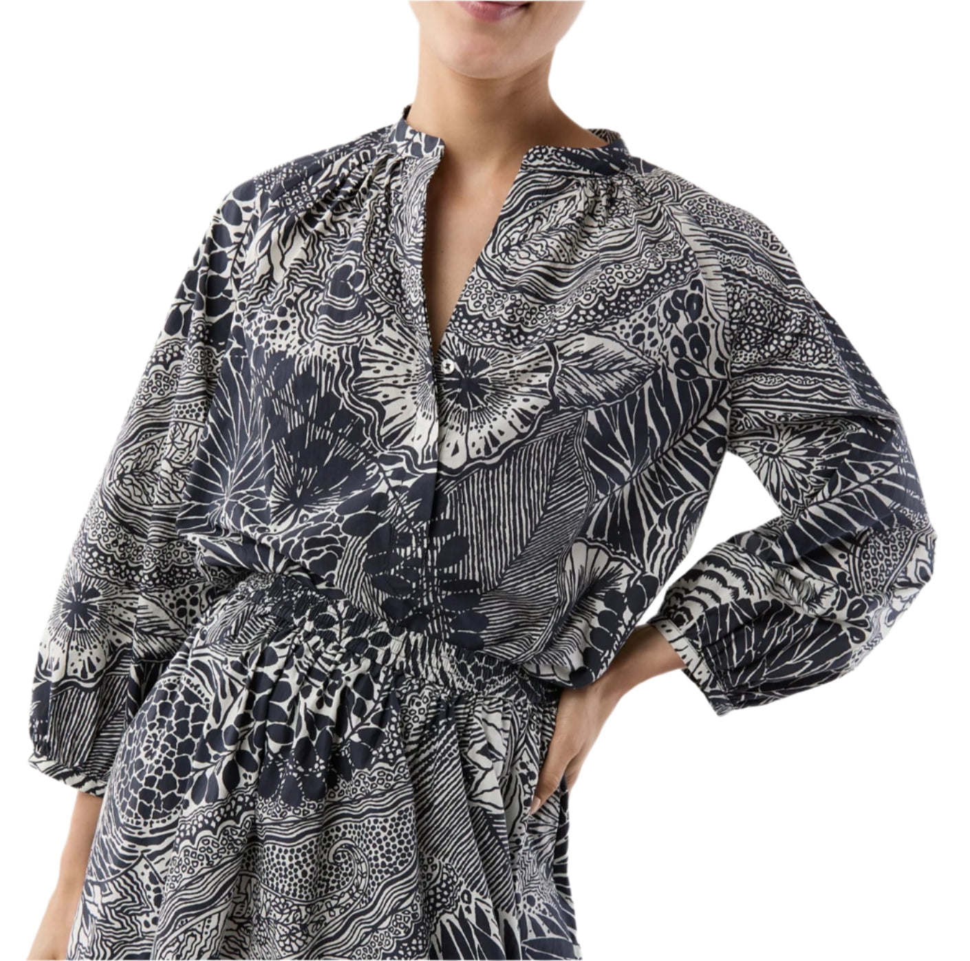 A person wearing the Ann Mashburn Sienna Block Print Top, a romantic black and white peasant blouse with long sleeves, a gathered waist, and V-neckline, rests their hand on their hip.