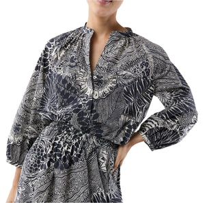 A person wearing the Ann Mashburn Sienna Block Print Top, a romantic black and white peasant blouse with long sleeves, a gathered waist, and V-neckline, rests their hand on their hip.