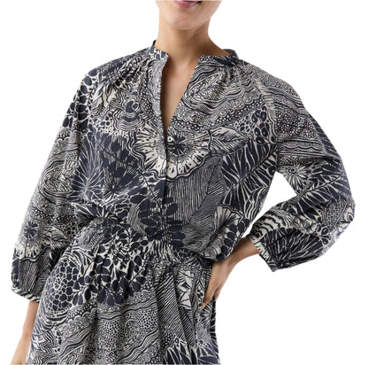 A person wearing the Ann Mashburn Sienna Block Print Top, a romantic black and white peasant blouse with long sleeves, a gathered waist, and V-neckline, rests their hand on their hip.
