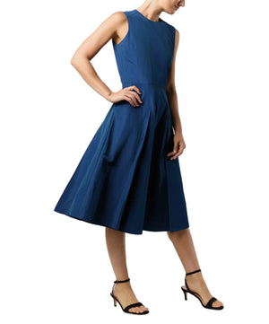 A person wearing the Arielle Dress by Ann Mashburn, a sleeveless, knee-length blue fit-and-flare dress with a fitted bodice and paneled skirt, paired with black strappy heels.