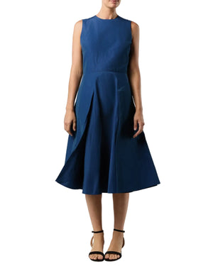 A woman wears the Ann Mashburn Arielle Dress, a sleeveless, knee-length navy fit-and-flare style with a fitted bodice and paneled skirt, paired with black ankle-strap sandals.