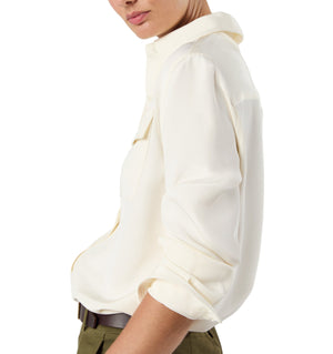 A person wearing the Ann Mashburn Hannah Blouse, a long-sleeve off-white utilitarian top with rolled-up sleeves, paired with olive green pants, shown in a side view.