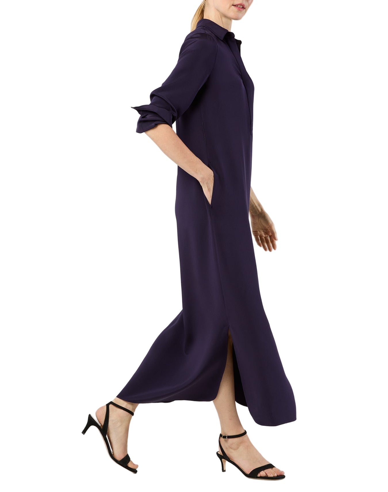 A person wearing the Ann Mashburn Piper Maxi Dress in dark purple crepe de chine with long sleeves, side slits, and black heeled sandals walks against a white background.